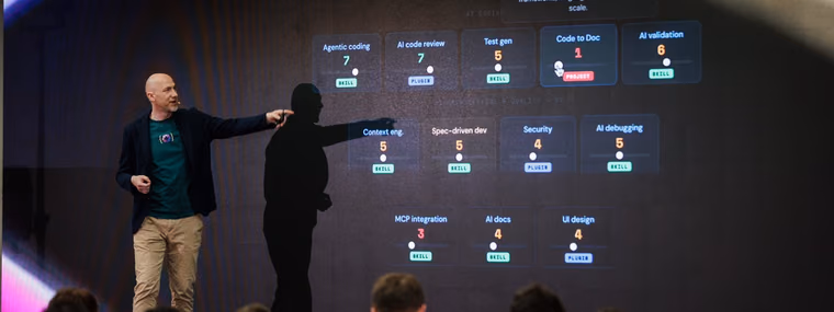 A speaker on the ELC Conference stage pointing at a screen of skill ratings for agentic coding and AI code review, the skills an AI engineering manager is now hired for.