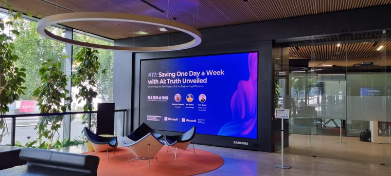 A lobby screen announcing an Engineering Leaders Community meetup on AI and engineering efficiency, with empty lounge chairs waiting for the room to fill.