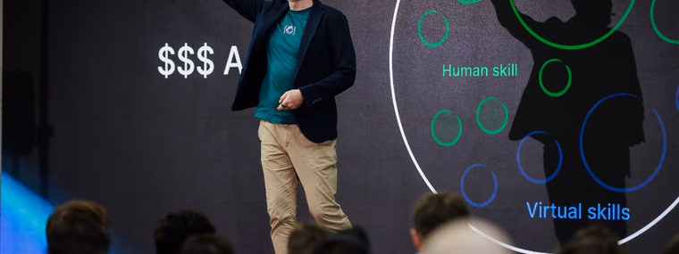 A speaker at the ELC Conference raising his arm beside a slide of overlapping circles labelled human skill and machine skill, the split an AI engineering manager has to staff for.