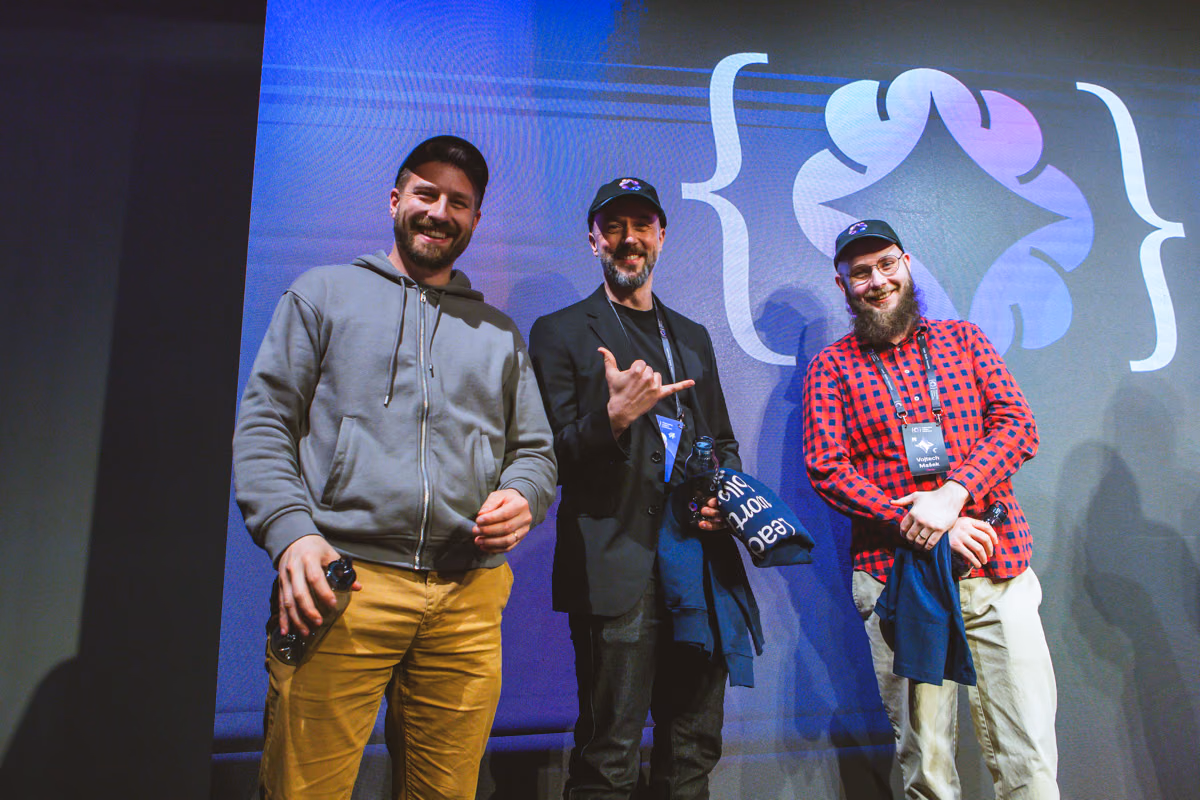 Three speakers smiling on the ELC Conference stage in front of the ELC bracket logo on the big screen