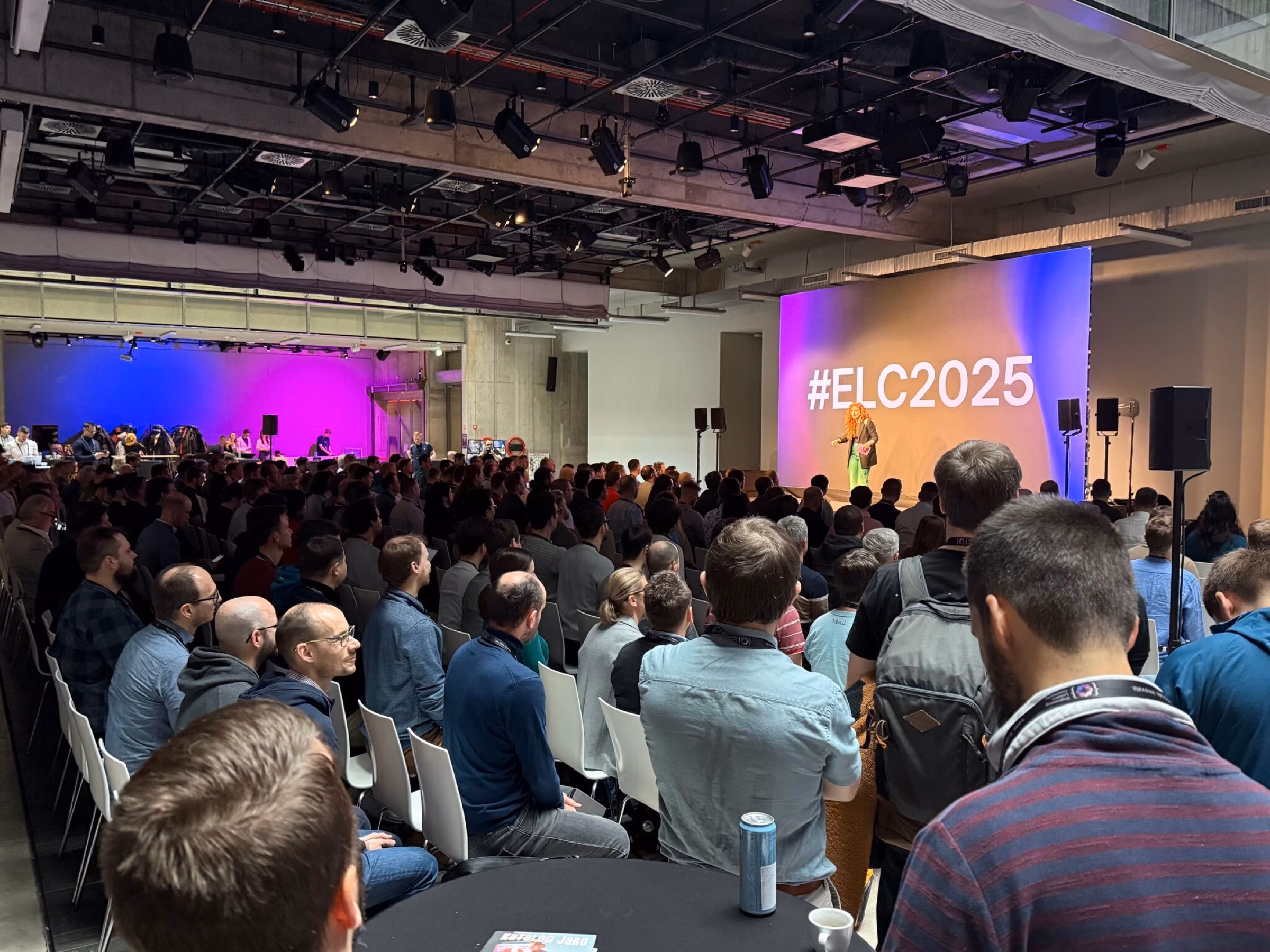 A packed conference room with a speaker in front of the giant ELC Conference screen, the stage the conference abstracts aim at