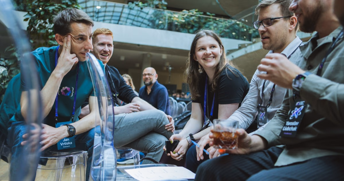 Skupina CTO a team leaderů se směje na průhledných židlích při networkingu na akci ELC, chvíle po dobré icebreaker hře