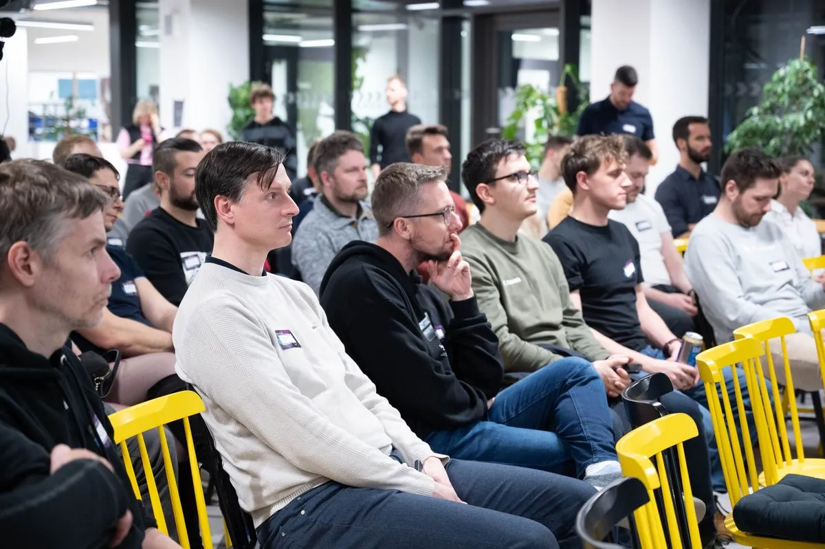 Řady engineering leaderů na žlutých dřevěných židlích poslouchají přednášku na ELC meetupu, další stojí u prosklených příček v pozadí.
