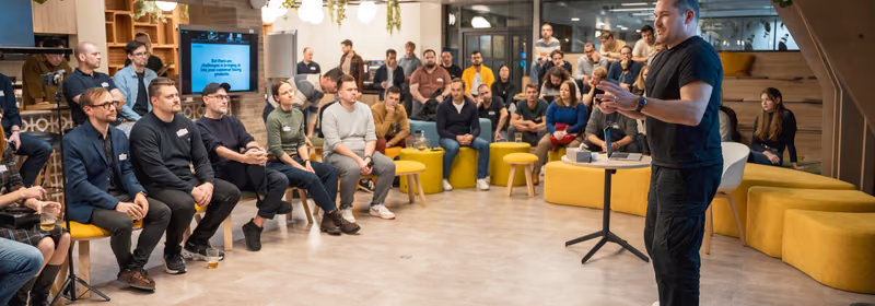 Řečník v černém tričku mluví k asi 40 sedícím IT manažerům na meetupu ELC, na plátně za ním nápis But there are challenges in bringing AI into your customer facing products.
