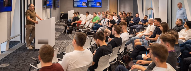 A speaker presenting from a podium beside multiple screens to a full room of engineering leaders at an ELC meetup, the audience a Head of AI hires from.