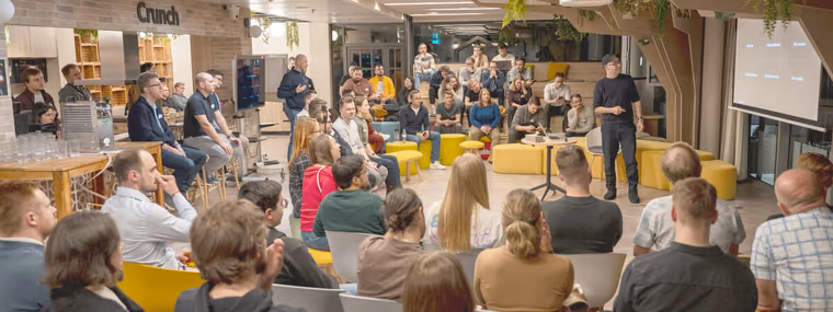 A speaker addressing a semicircle of seated engineering leaders in a plant-filled lounge at an ELC meetup, the kind of room where a Head of AI compares notes with peers.