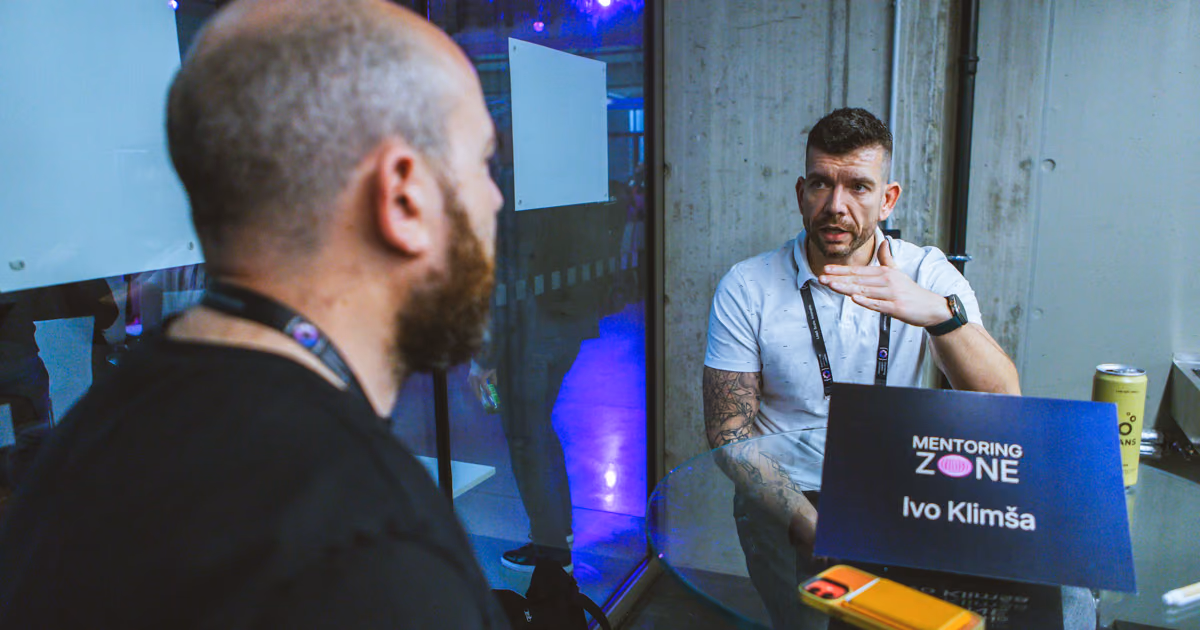 Two engineering leaders in a one-on-one conversation across a glass table in the Mentoring Zone at an ELC event, one explaining with his hand