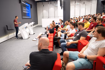 A speaker on stage at a monthly ELC meetup in front of a full auditorium of senior engineers and engineering leaders.