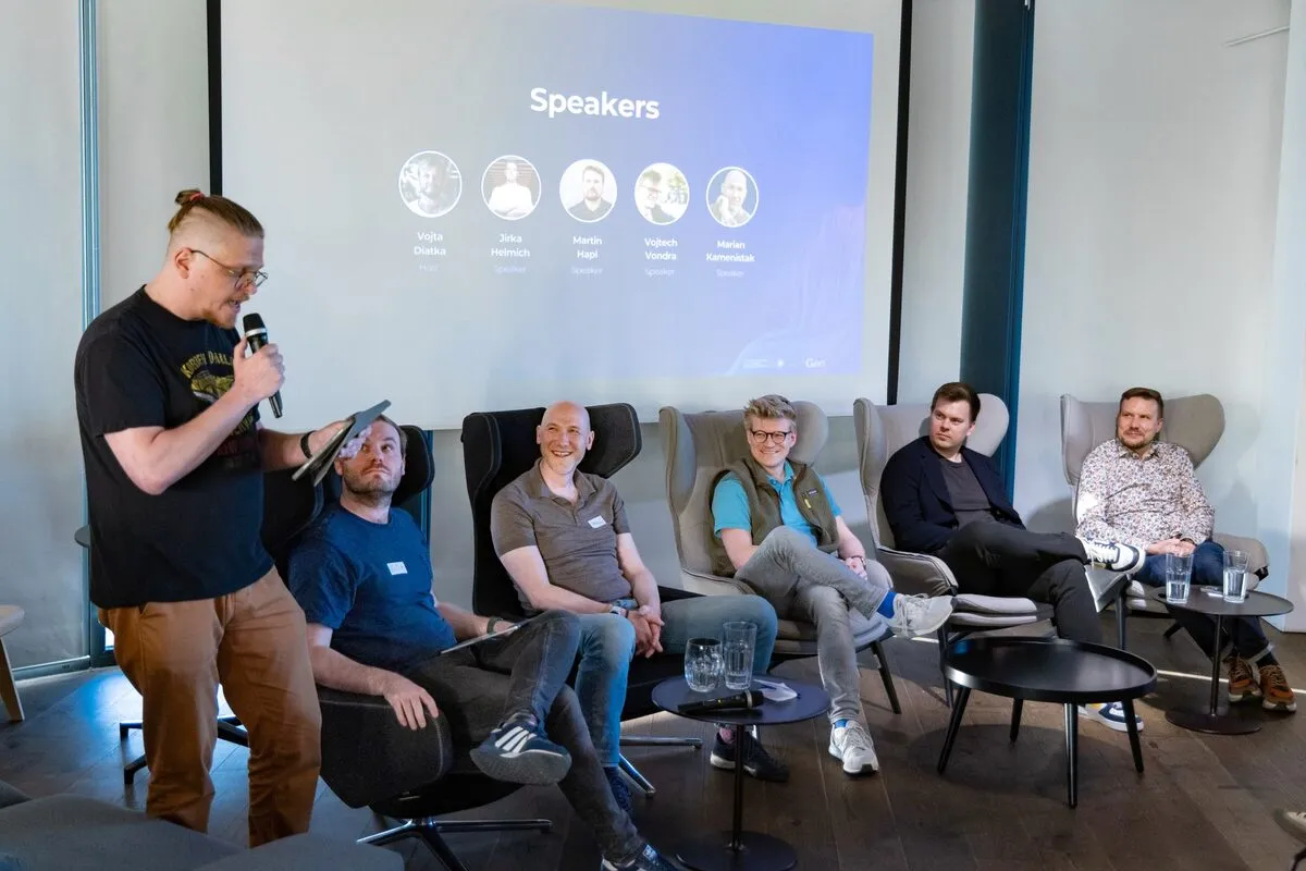 Moderátor s mikrofonem stojí vedle pěti sedících panelistů na ELC meetupu, před slidem s nadpisem Speakers.
