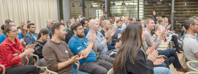 A large seated crowd of engineering leaders applauding at an ELC meetup in a room with glass walls, CTOs, engineering managers and staff engineers side by side.