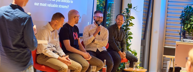 A moderator with a microphone in front of four seated panelists at an ELC meetup, a slide about the work of Staff Engineers projected behind them.