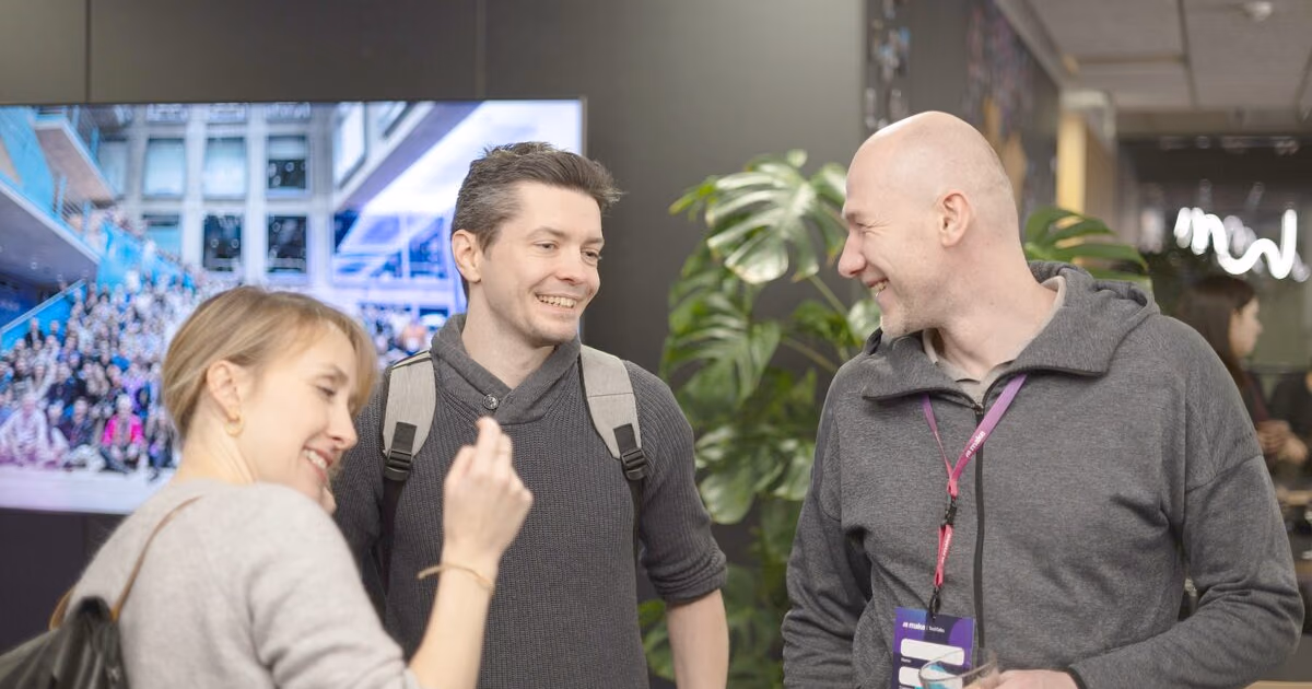 Three engineering leaders laughing together at an ELC meetup, one wearing an attendee lanyard