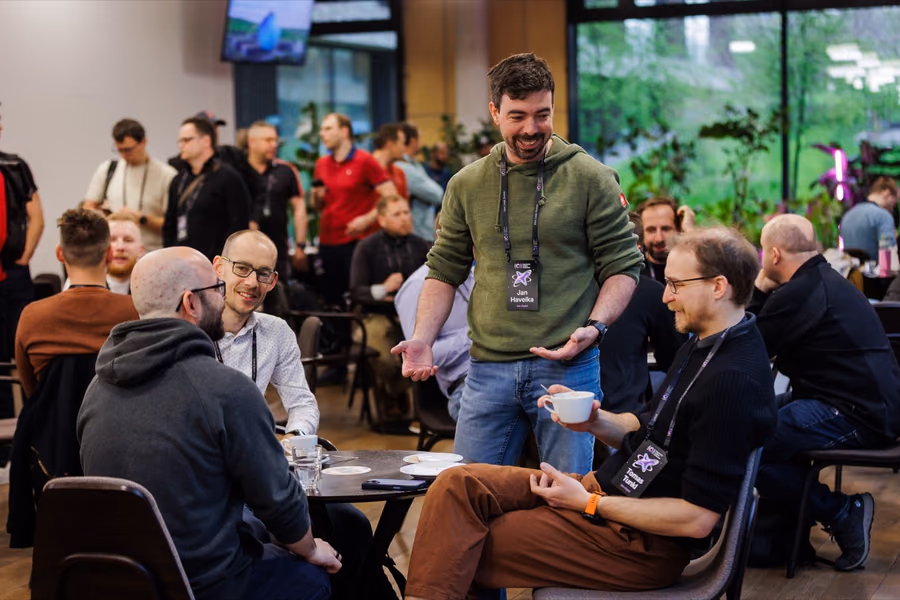 Engineering leaders talking at small round tables during a coffee break, one standing with a cup, the moment a good opener carries into