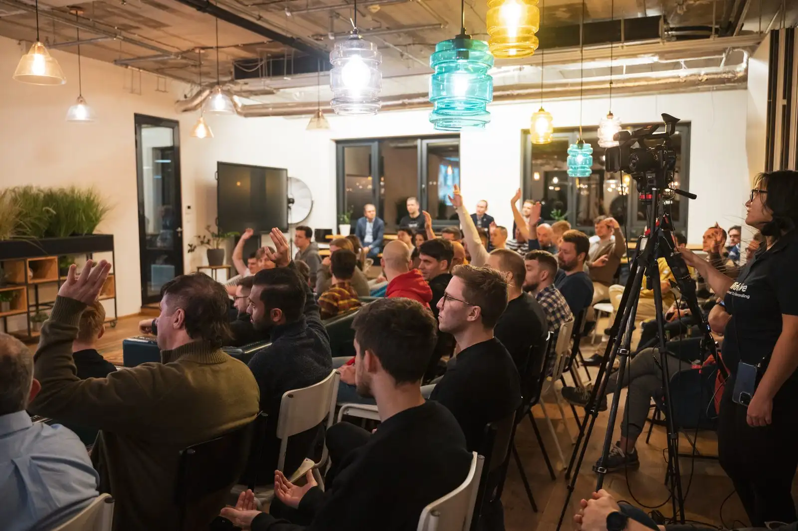 Two cameras on tripods filming an ELC meetup from the back of a full room.