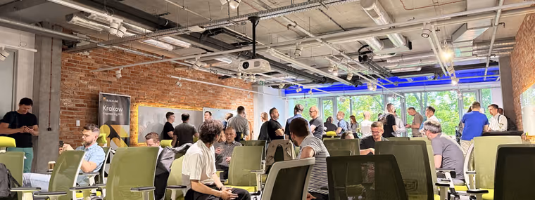 Engineering leaders standing and talking between green office chairs in a loft room with a brick wall at the ELC meetup in Kraków