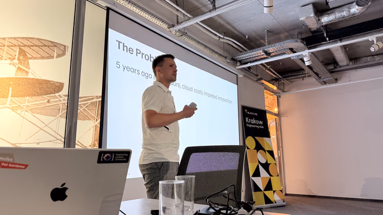 A speaker presenting slides next to a Krakow Engineering Hub roll-up banner at the ELC meetup in Kraków