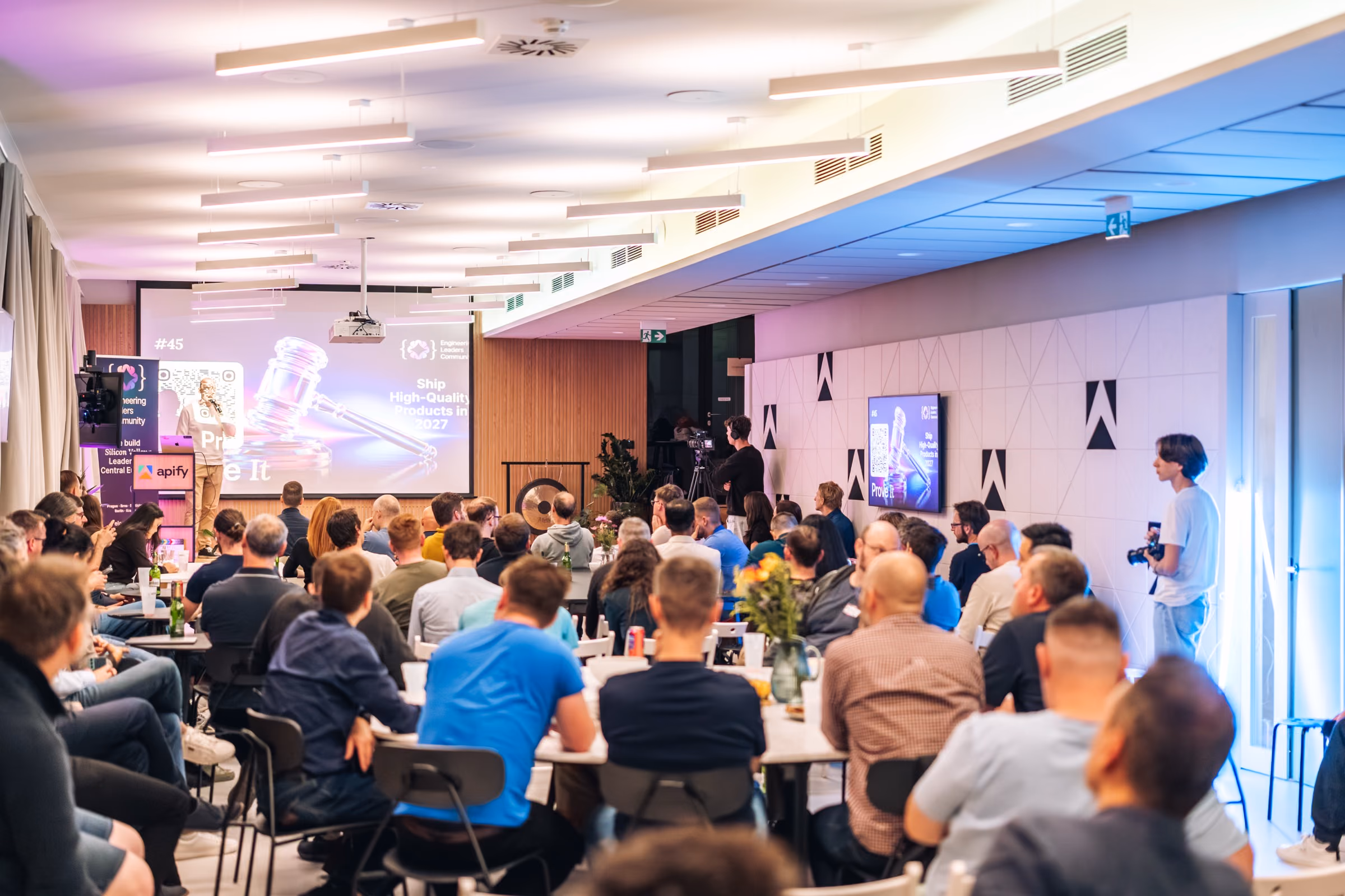 The full room of ELC meetup #43 at Apify from the back, the Apify roll-up by the stage and a camera on a tripod recording the talk
