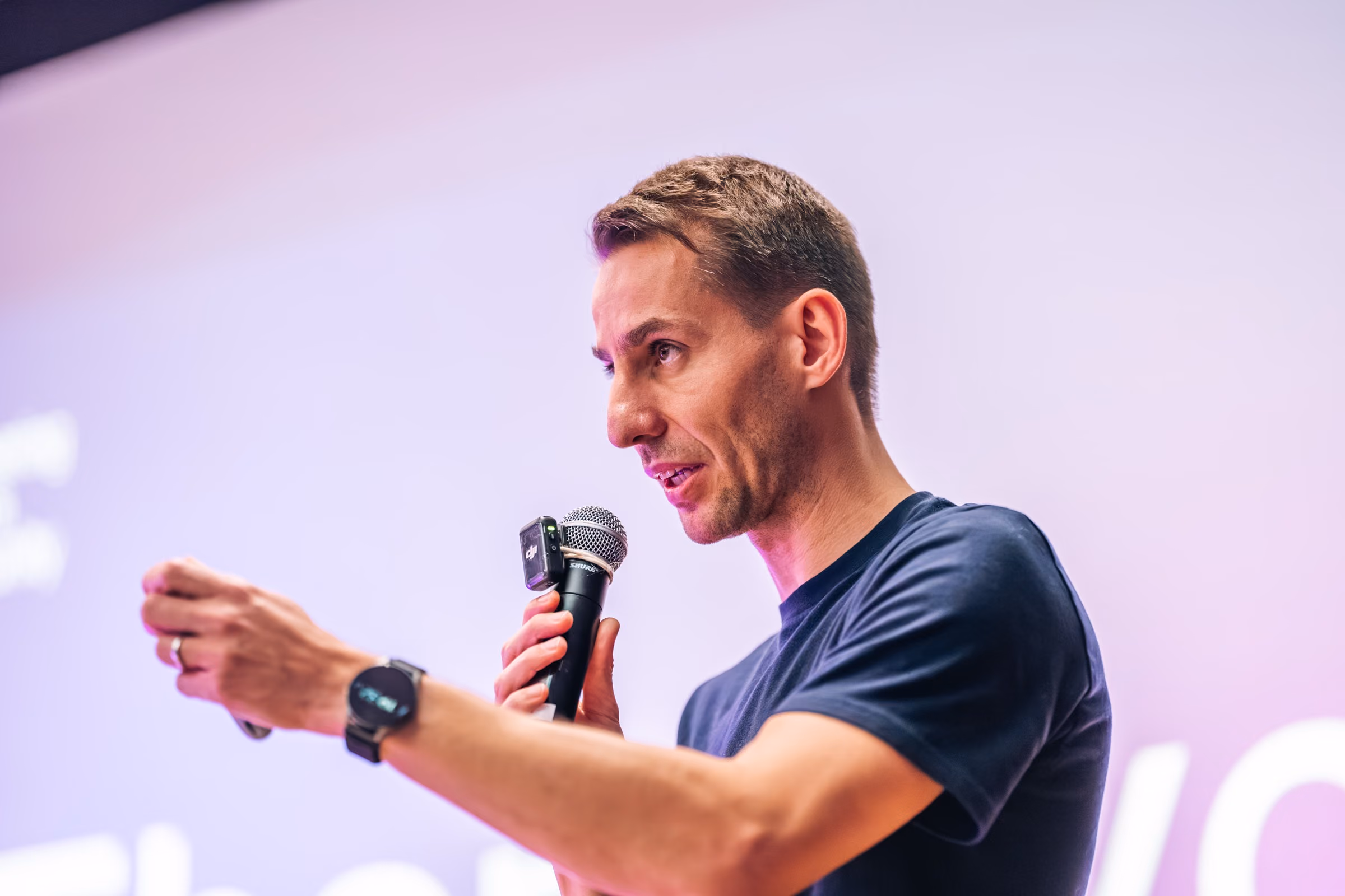 Jan Vrtiška mid-sentence with a microphone and an outstretched hand on the ELC meetup #43 stage at Apify