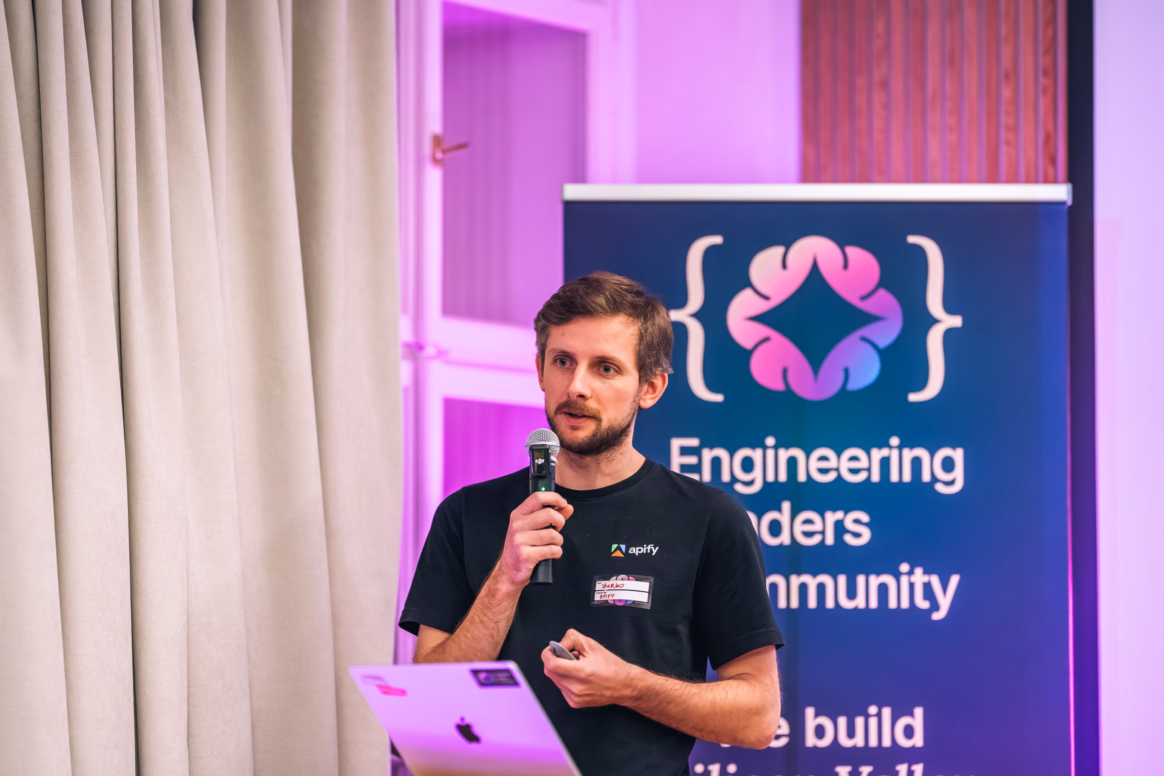 Yurko from Apify speaking with a microphone at ELC meetup #43 at Apify, the Engineering Leaders Community roll-up behind him, the stage a public speaking coach prepares your engineer for