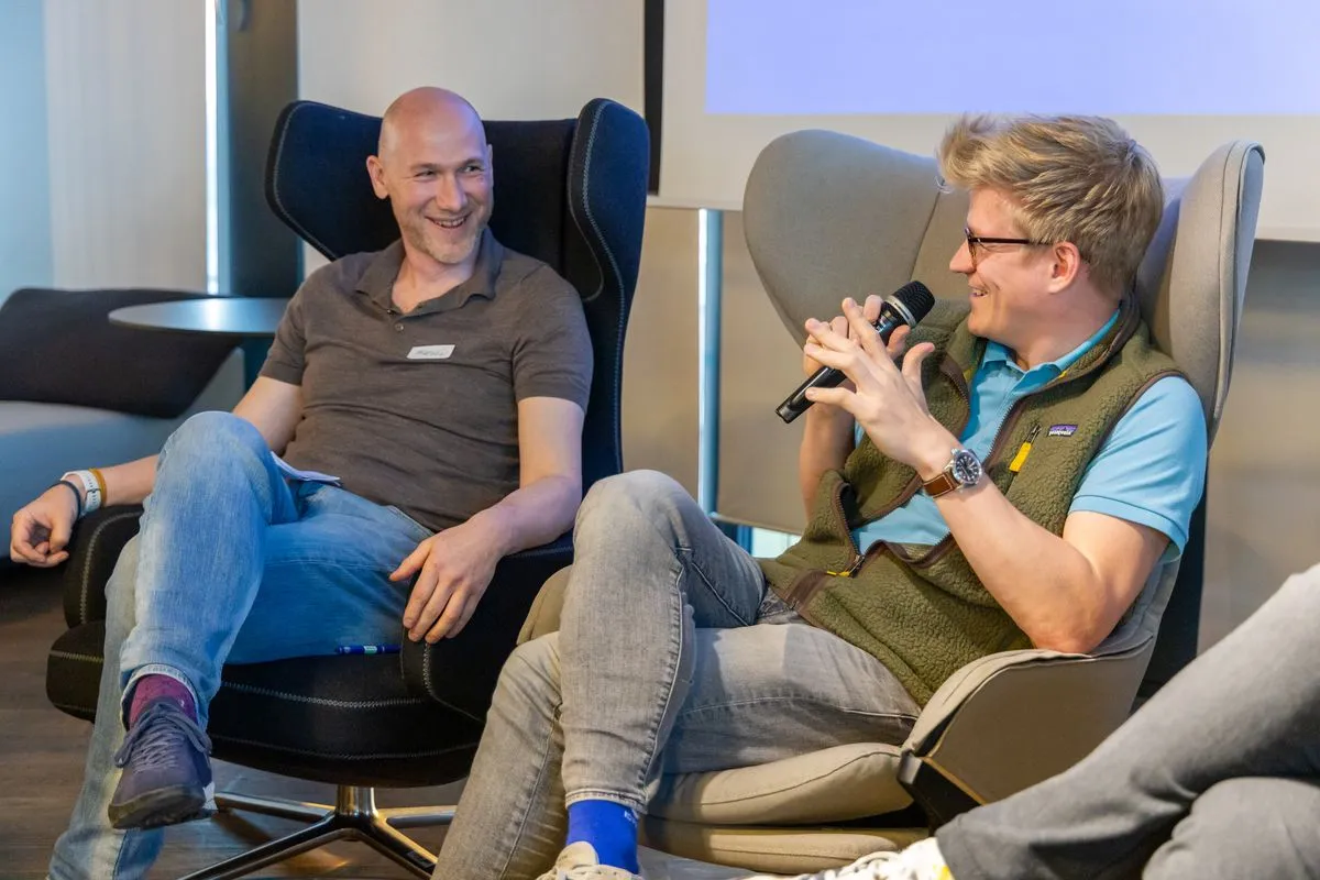 Two engineering leaders sitting in armchairs during a fireside-style chat at an ELC meetup, one speaking into a microphone while the other listens and smiles.