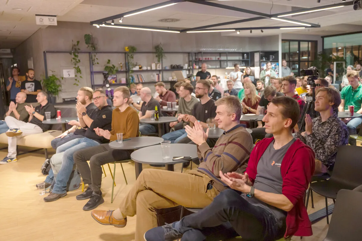 A packed ELC meetup audience seated at small round tables in a lounge venue, applauding a speaker, with more attendees standing at the back of the room.