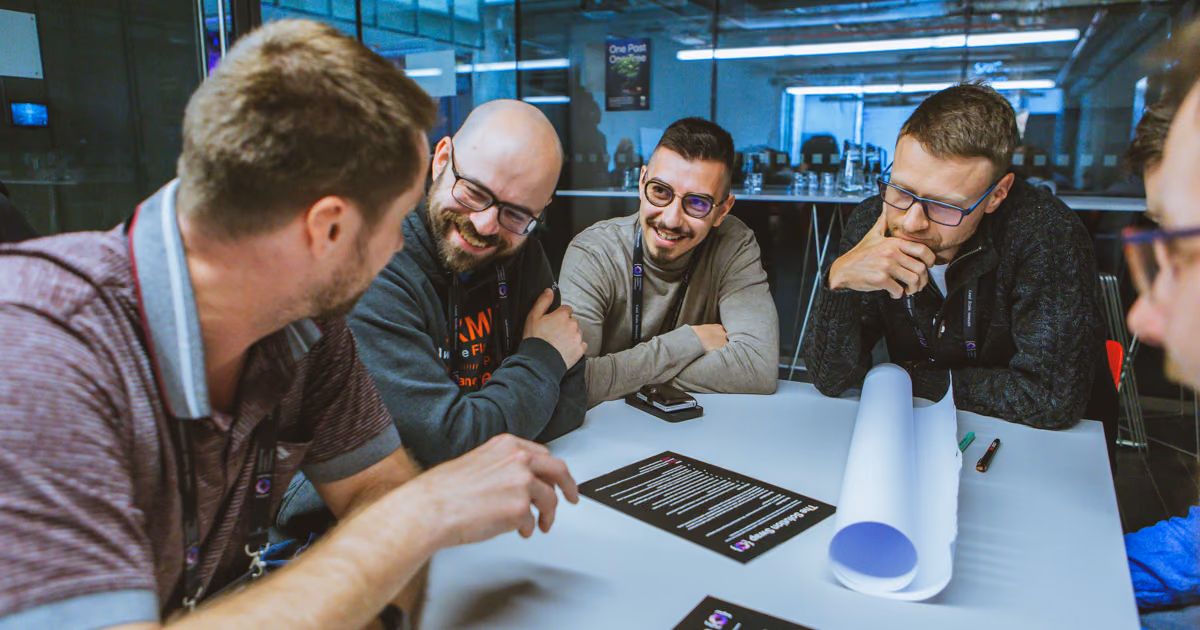 Five people around a white table with printed worksheets, laughing during an ELC workshop session