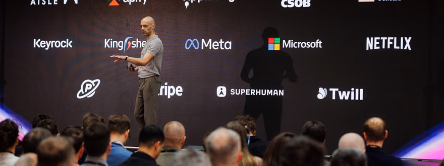 Řečník na pódiu ELC konference před velkou obrazovkou s logy firem včetně Apify, Meta, Microsoft, Netflix a Stripe, v popředí sedící publikum.