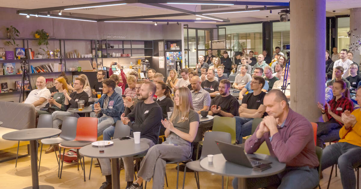 A packed ELC meetup audience seated at small round tables applauding under string lights