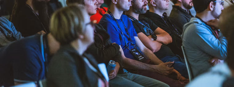 A wide shot of a large seated audience at the ELC Conference, rows of attendees wearing lanyards, watching a talk intently.