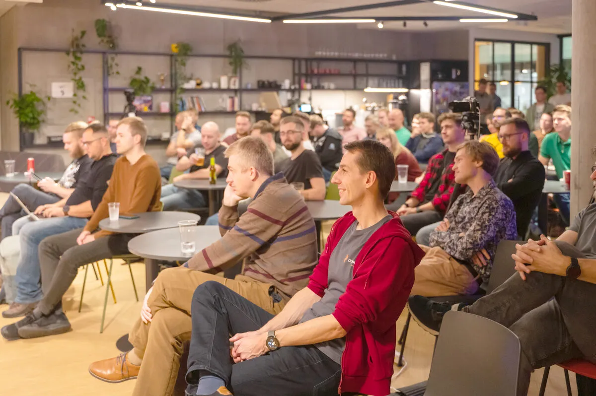 A large ELC meetup audience listening attentively in a modern lounge-style venue with plants and shelving.